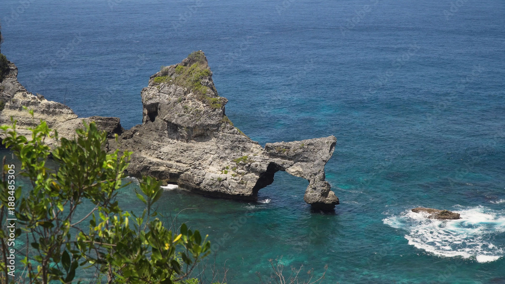 Rock in the ocean at Atuh beach on Nusa Penida island, Indonesia. Rocks in a blue sea lagoon with breaking waves. Travel concept