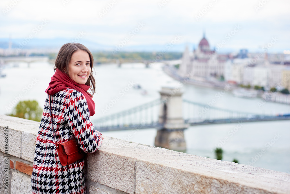 Close-up of a nice female looking back at the camera with smile against beautiful view of the Hungarian Parliament and the chain bridge in Budapest, Hungary. Blurred background