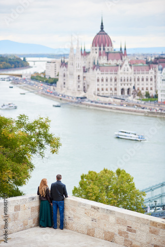 Elegant pair is enjoying each other on the background of Danube River and Parliament Building in Budapest, Hungary. Blurred background © anatoliy_gleb