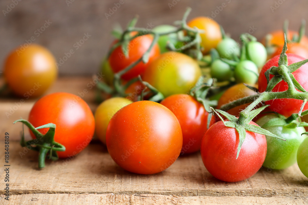 Fresh small tomatoes with green stem on wooden background