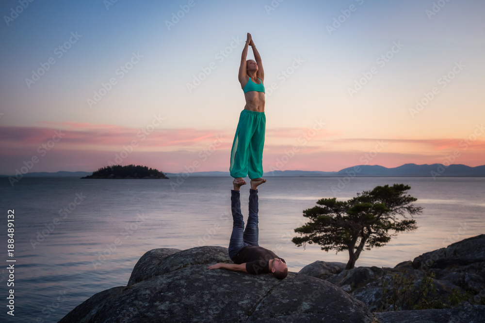A beautiful couple of young people, man and woman, are doing Acro Yoga together in nature during a colorful summer sunset. Taken in Whytecliff Park, Horseshoe Bay, West Vancouver, BC, Canada.