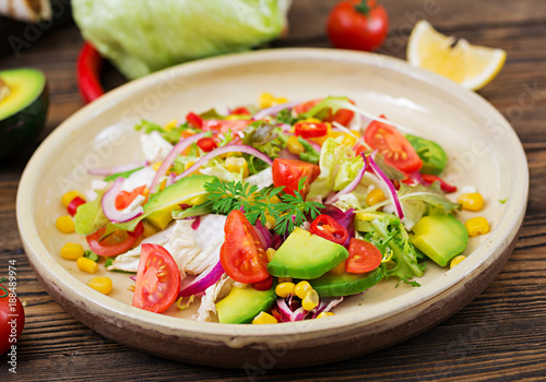 Appetizing vegan salad from tomatoes, avocado, corn, red onion and lettuce leaves. Tasty vegan food. Healthy vegan food. Vegetarian salad.