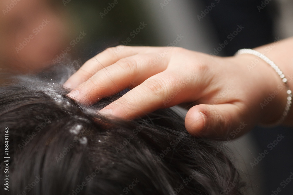 Naklejka premium Female hand puts powder for volume on dark hair, close-up.