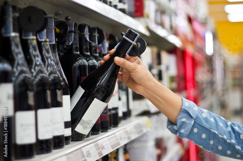 Woman is buying a bottle of wine in supermarket background