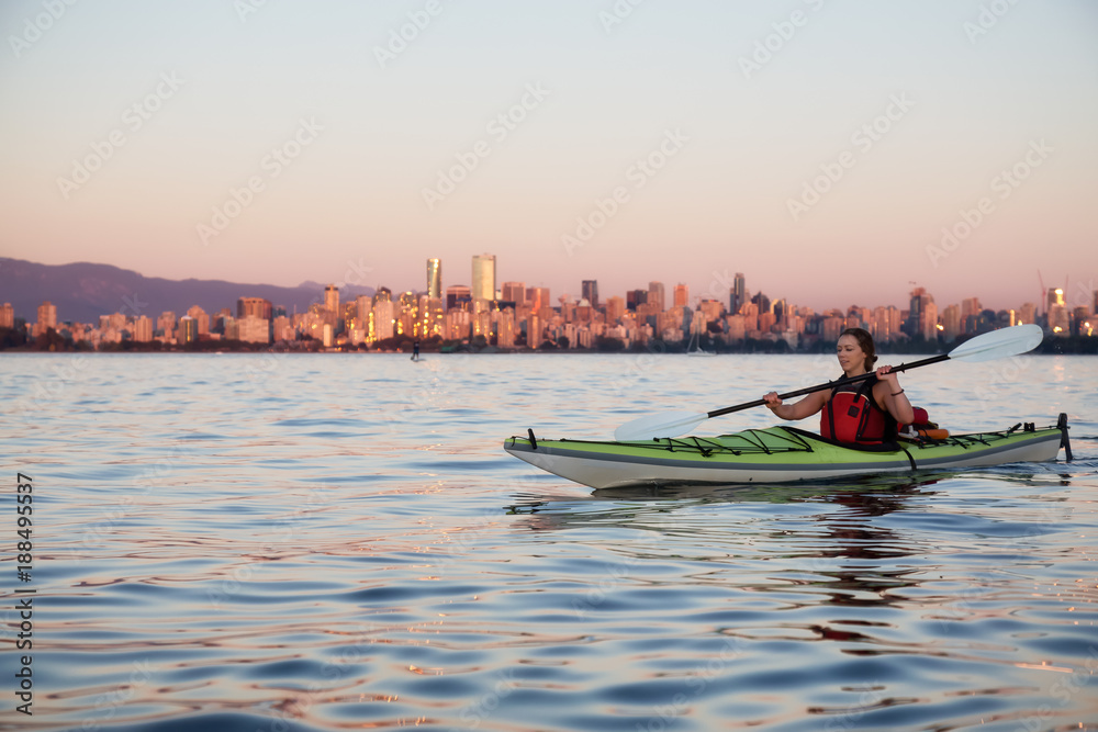 Woman Kayaking on a kayak during a vibrant Sunset with city skyline in the background. Taken in Vancouver, British Columbia, Canada.