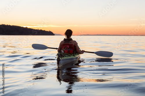 Adventure Girl kayaking on a sea kayak during a colorful and vibrant sunset. Taken near Jericho Beach, Vancouver,