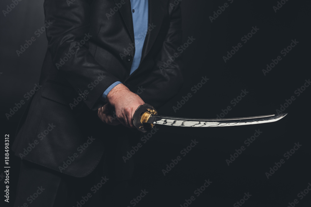 cropped shot of man in suit holding japanese katana sword on black Stock  Photo | Adobe Stock