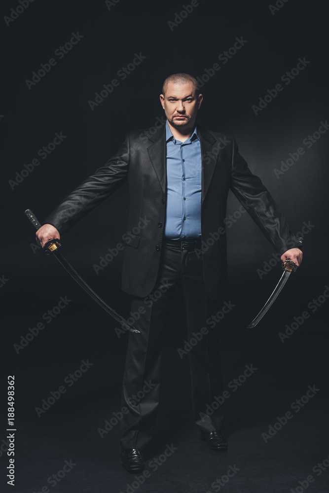 handsome serious man in suit with dual katana swords on black