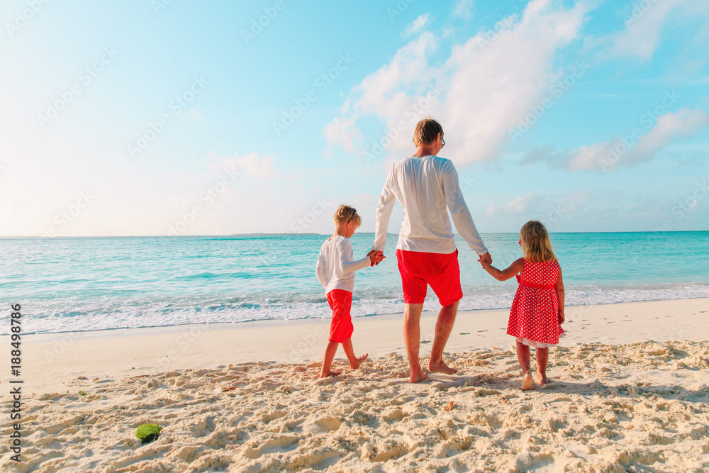 father and two kids walking on beach