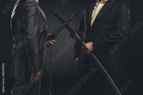 cropped shot of meeting of modern samurai in suits with katana swords isolated on black