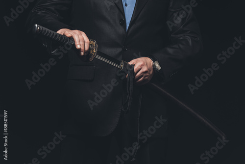 cropped shot of man in suit taking out his katana sword isolated on black