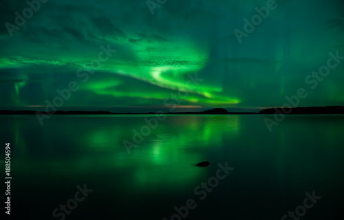 Northern lightd dancing over calm lake in Farnebofjarden national park in Sweden.