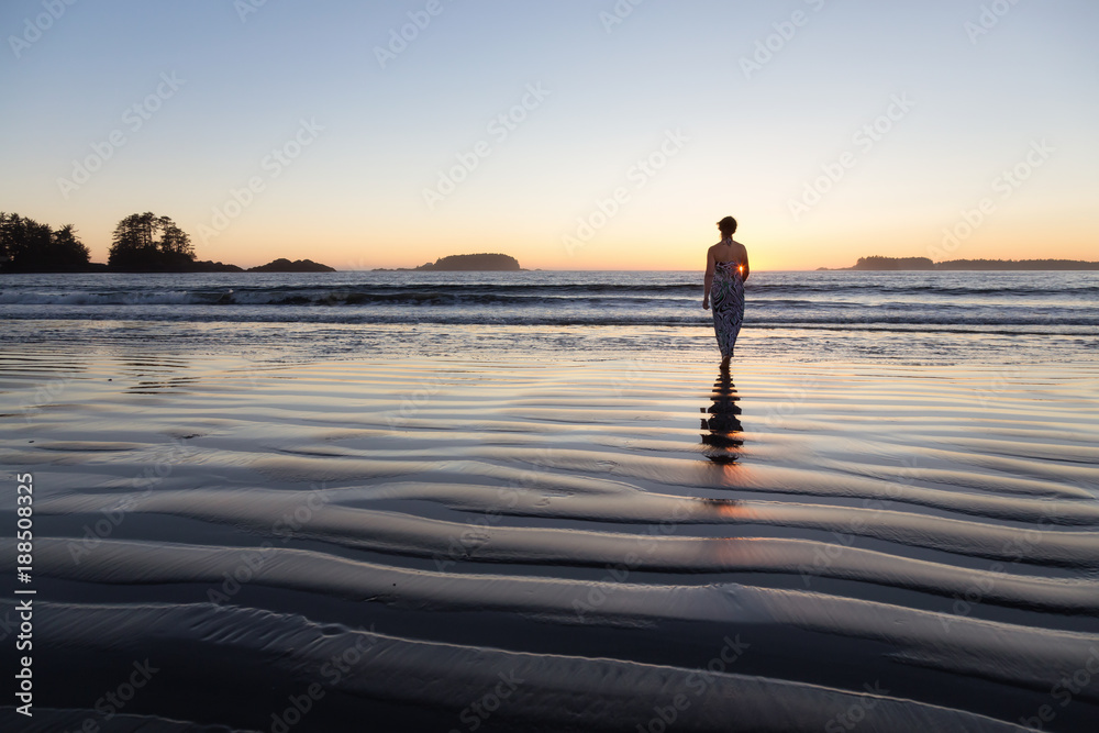 Woman Walking on a Sandy Beach during a vibrant and colorful summer sunset. Taken in Tofino, Vancouver Island, BC, Canada.