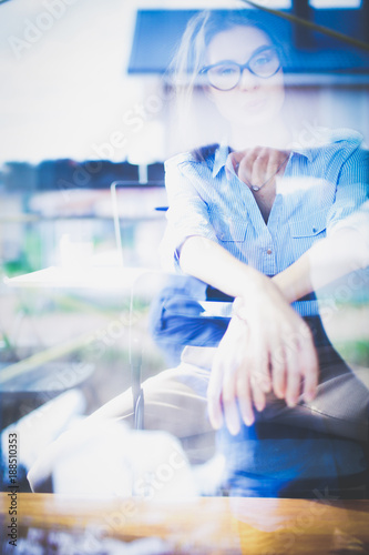 Young woman sitting at office table with laptop,view through window. Young woman