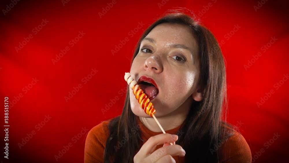 A sexy European woman sensually eats lollipop on a red background. A sexy European woman sensually eats lollipop on a red background.