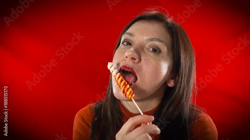 A sexy European woman sensually eats lollipop on a red background. photo