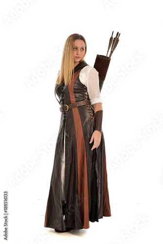 full length portrait of girl wearing brown fantasy costume, holding a bow and arrow. standing pose on white studio background. 