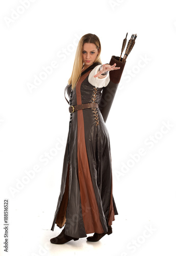 full length portrait of girl wearing brown fantasy costume, holding a bow and arrow. standing pose on white studio background. 
