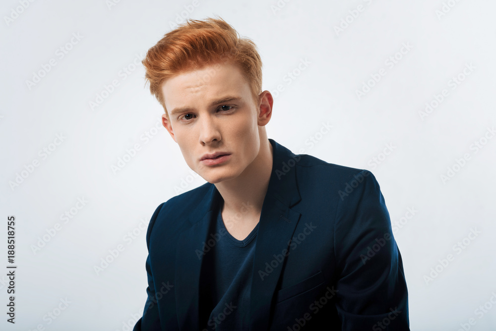 Haircut. Handsome stony-faced red-haired young man wearing a black jacket and staring and having a modern haircut Haircut. Handsome stony-faced red-haired young man wearing a black jacket and staring and having a modern haircut
