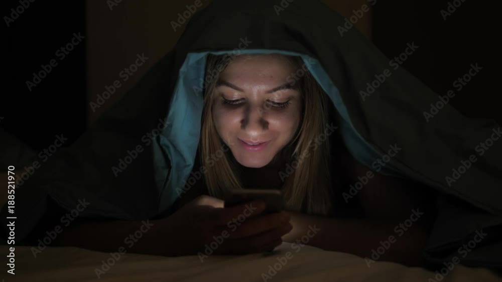 At Night In Dark Cute Woman Using Mobile Phone And Lying On Bed Under Blanket At Night In Dark Cute Woman Using Mobile Phone And Lying On Bed Under Blanket