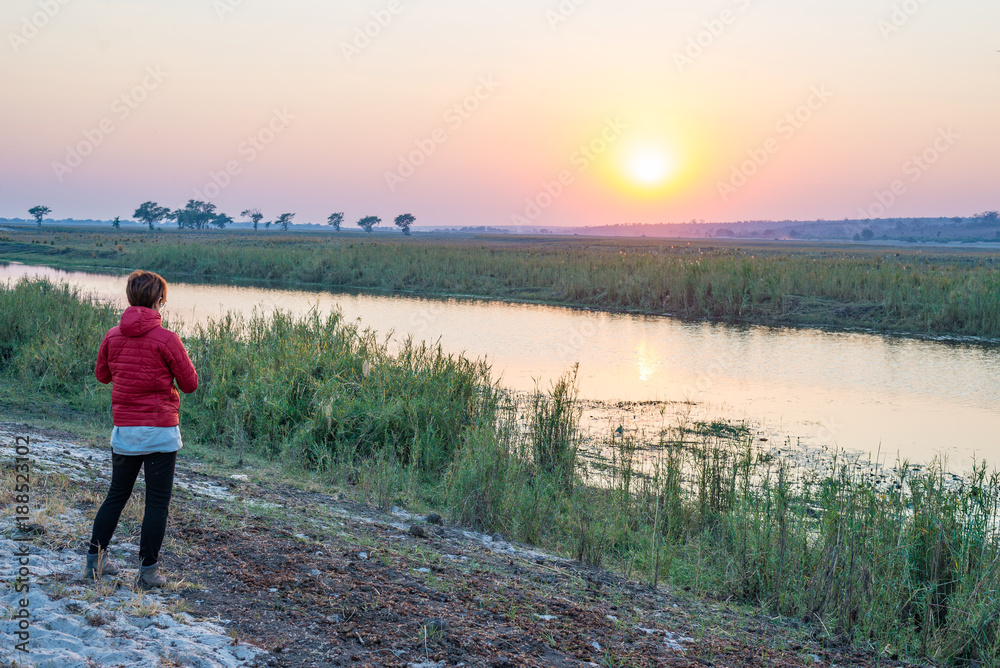 Tourist looking at sunrise over Chobe River, Namibia Botswana Africa. Natural colors, rear view.