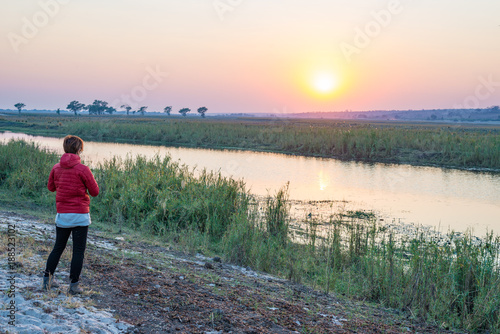 Tourist looking at sunrise over Chobe River, Namibia Botswana Africa. Natural colors, rear view.