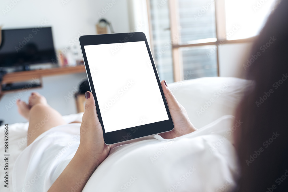 Mockup image of woman's hands holding black tablet pc with blank desktop white screen while lying in a white bed Mockup image of woman's hands holding black tablet pc with blank desktop white screen while lying in a white bed
