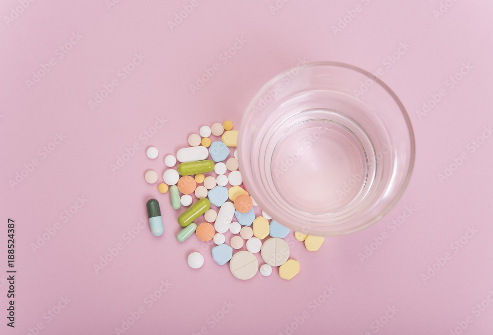 colorful medicine and glass of water on pink background.