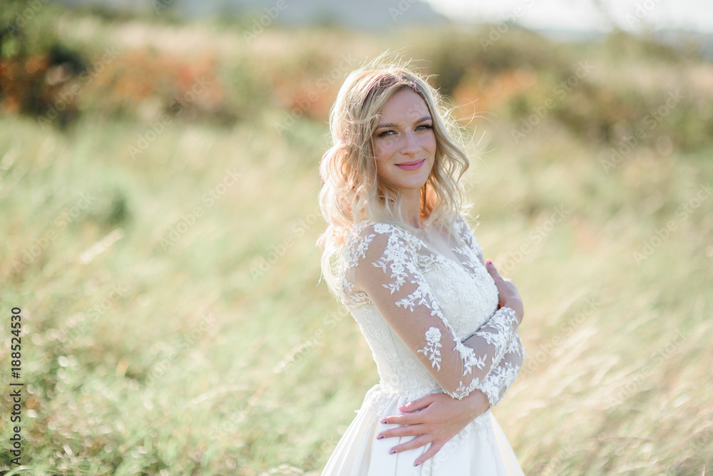 Stunning bride with white curls stands on the field in a sunny day Stunning bride with white curls stands on the field in a sunny day