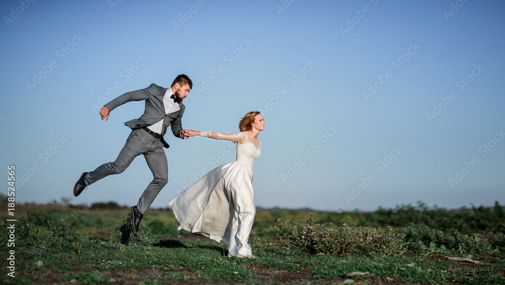 Joyful wedding couple runs against the wind across the field