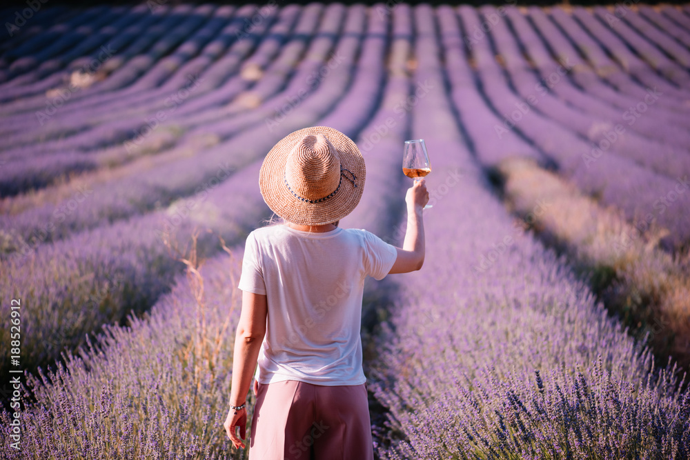 Obraz premium Młoda kobieta pije wino różane w polu lawendy słońca, stojąc z powrotem do kamery, Provence, południowej Francji