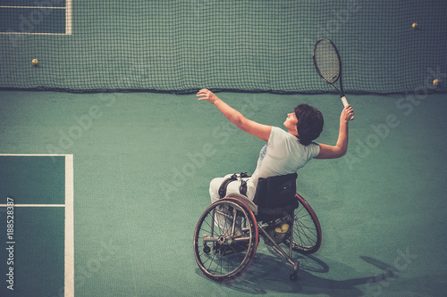 Disabled mature woman on wheelchair playing tennis on tennis court photo