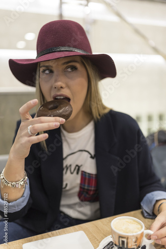 Woman with hat eating donut and hot beverage in bar