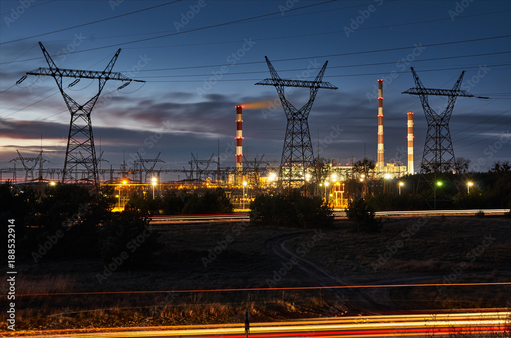 Illuminated power plant with chimneys and poles at night.