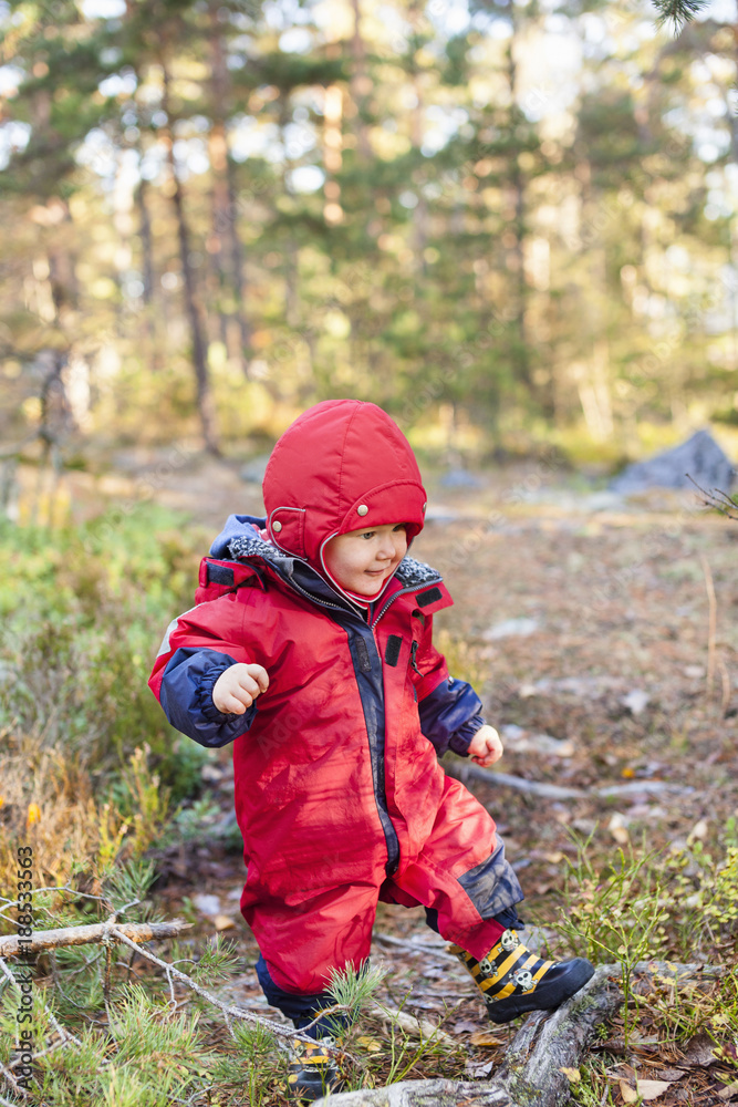 Little baby boy in red snowsuit walking in forest Little baby boy in red snowsuit walking in forest