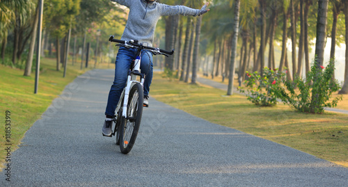 woman cyclist riding bike with outstretched arms in tropical park