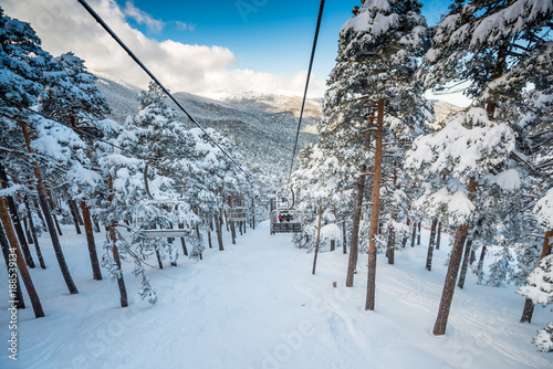 A winter view of a ski resort full of fresh snow taken from the chairlift going through a forest, in Madrid, Spain