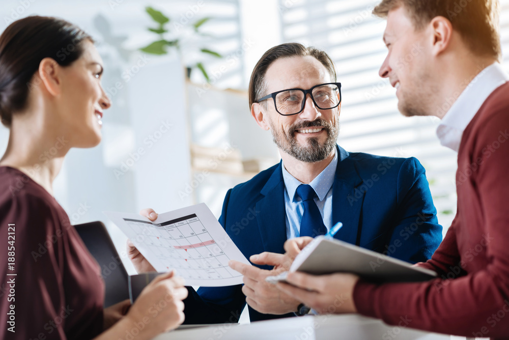 Team cooperation. Low angle of happy optimistic three colleagues achieving new goal while smiling and looking at each other 