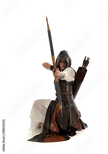full length portrait of girl wearing brown fantasy costume, holding a bow and arrow, on white studio background. 