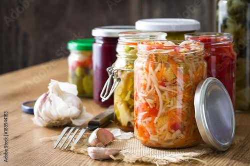 Fermented preserved vegetables in jar on wooden table. Copyspace photo