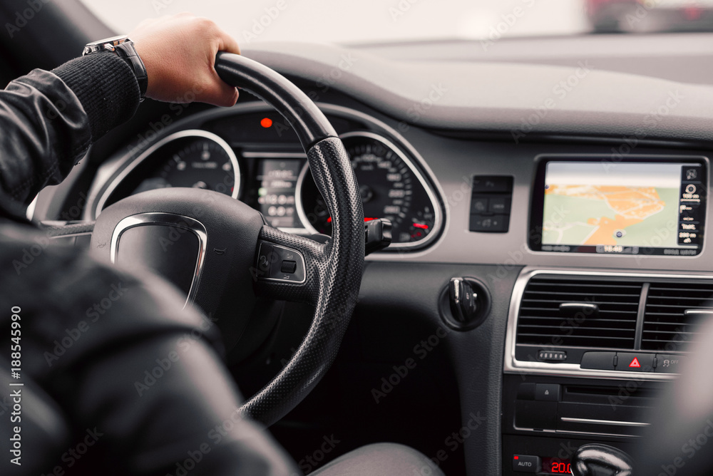 Businessman driving luxury modern car in the city. Close up man's hand on the wheel of the car.