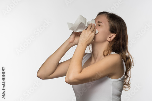 A beautiful brunette woman becomes ill with a cold and runny nose, sneezes and coughs into a white paper kerchief