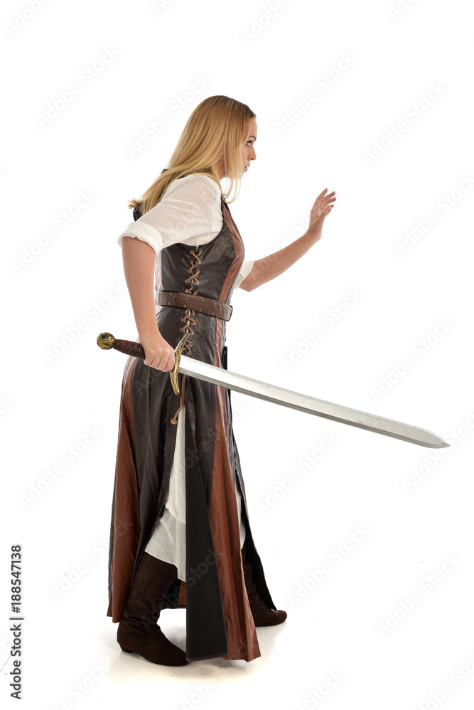 full length portrait of girl wearing brown fantasy costume, holding a sword. standing pose on white studio background. full length portrait of girl wearing brown fantasy costume, holding a sword. standing pose on white studio background.