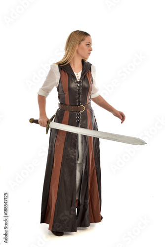 full length portrait of girl wearing brown fantasy costume, holding a sword. standing pose on white studio background. 