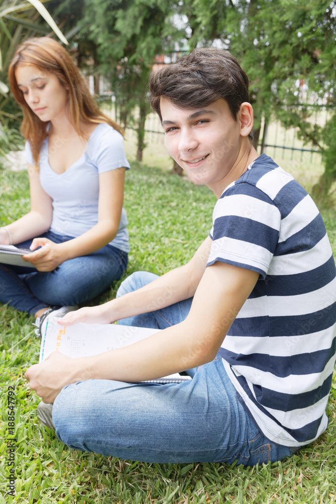 Couple of teenagers happy outdoor making school tests seated on the grass Couple of teenagers happy outdoor making school tests seated on the grass