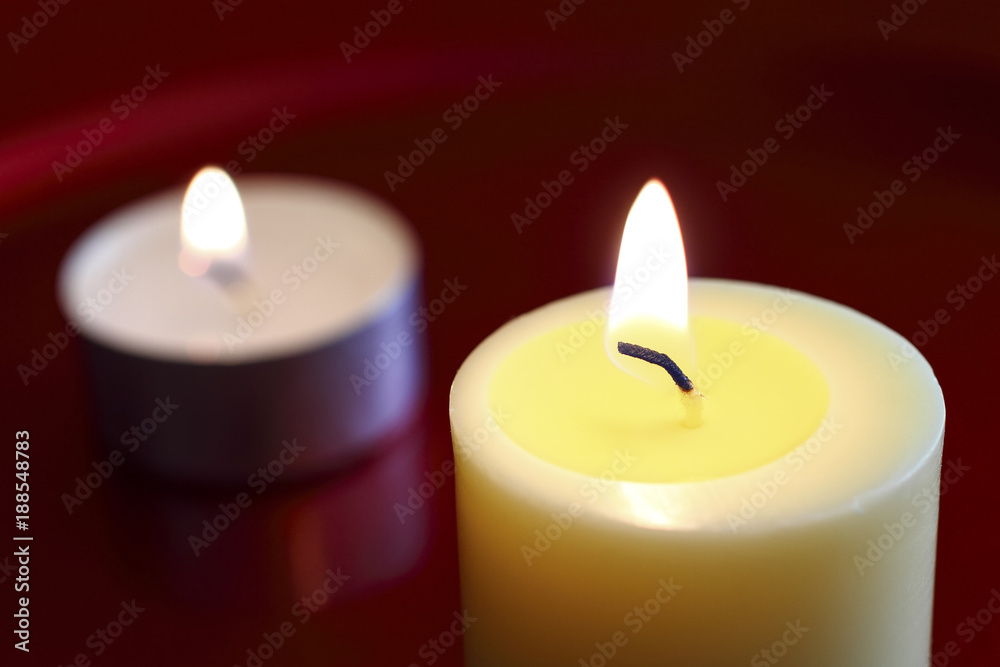 .Close up of a burning wax candle against a red background. .Close up of a burning wax candle against a red background.