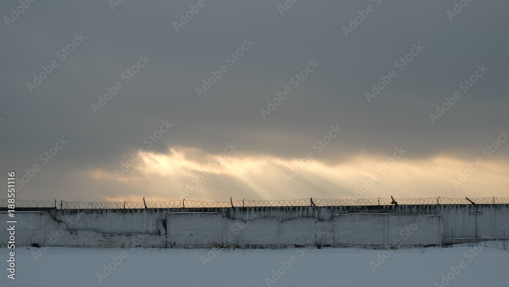 The rays of the sun break through the gray sky on the background of a fence with a barbed wire.