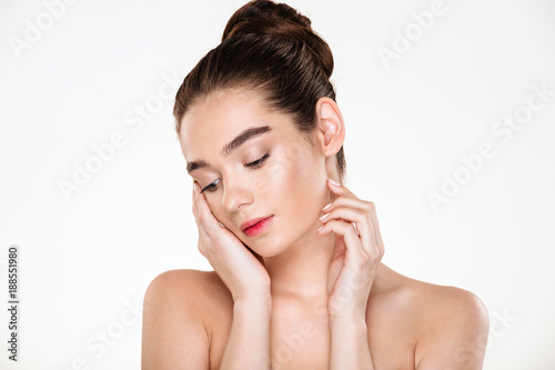 Horizontal portrait of tender woman being half-naked posing over white background with face downward touching her face