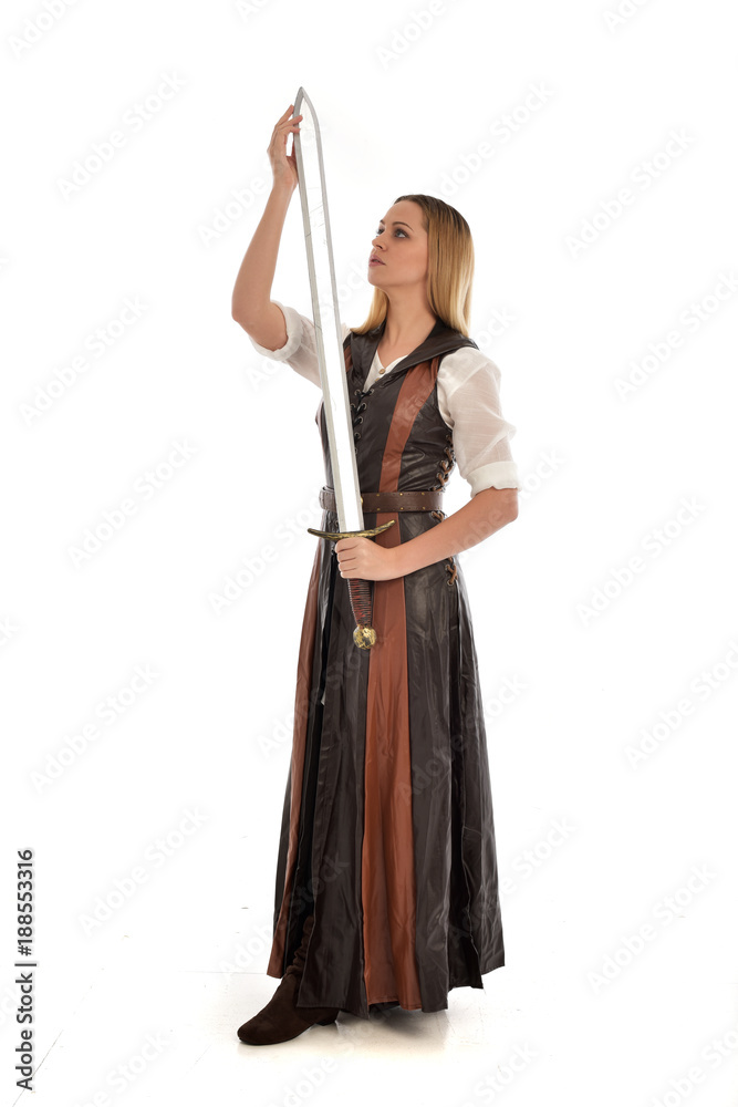 full length portrait of girl wearing brown fantasy costume, holding a sword. standing pose on white studio background. full length portrait of girl wearing brown fantasy costume, holding a sword. standing pose on white studio background.