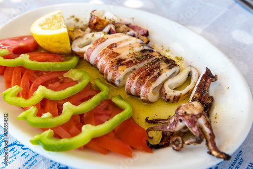 Seafood, grilled calamari served with tomatoes, green peppers and lemon in traditional Greek tavern. Naxos island. Greece.